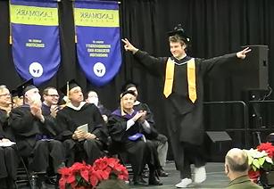 graduating student walking to podium with arms spread wide in celebration
